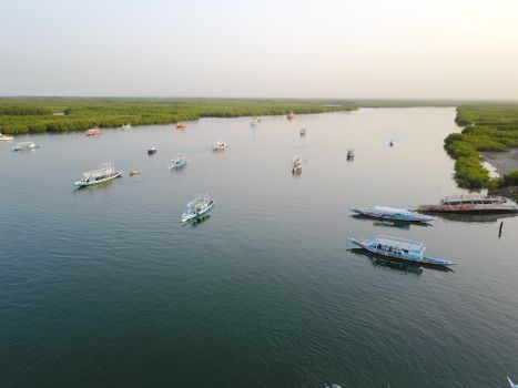 Vue aérienne de bateaux de pêche sur une rivière en Gambie entourée d'une végétation luxuriante, pendant la journée.
