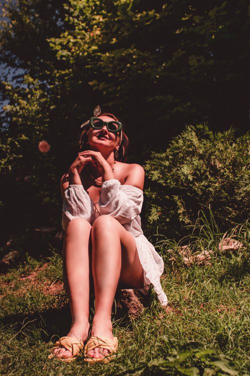 Free Woman enjoying a sunny day outdoors, wearing sunglasses and a white dress. Summer vibes. Stock Photo