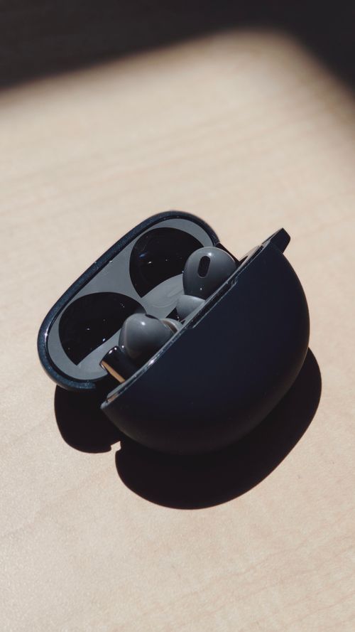 Free Close-up of sleek black wireless earbuds in open charging case on wooden table. Stock Photo