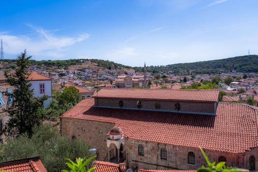 Explore Ayvalık's charming red-tiled roofs and scenic hills under a bright sky.