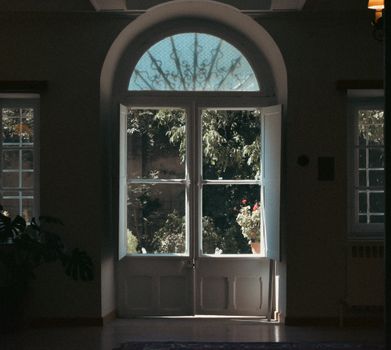 An elegant arched window opens to a lush garden view, casting serene light indoors.