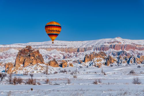Free Captivating hot air balloon floating above snow-covered Cappadocia rock formations in Turkey. Stock Photo