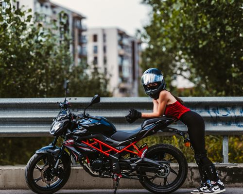 Free Female motorcycle rider in gear poses beside bike on urban roadside, showcasing modern biking culture. Stock Photo