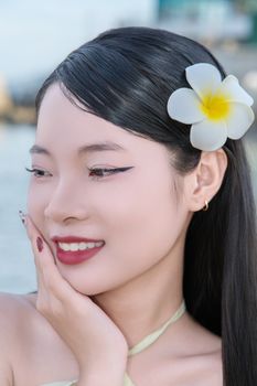 Close-up of a smiling woman with a flower in her hair near the water.