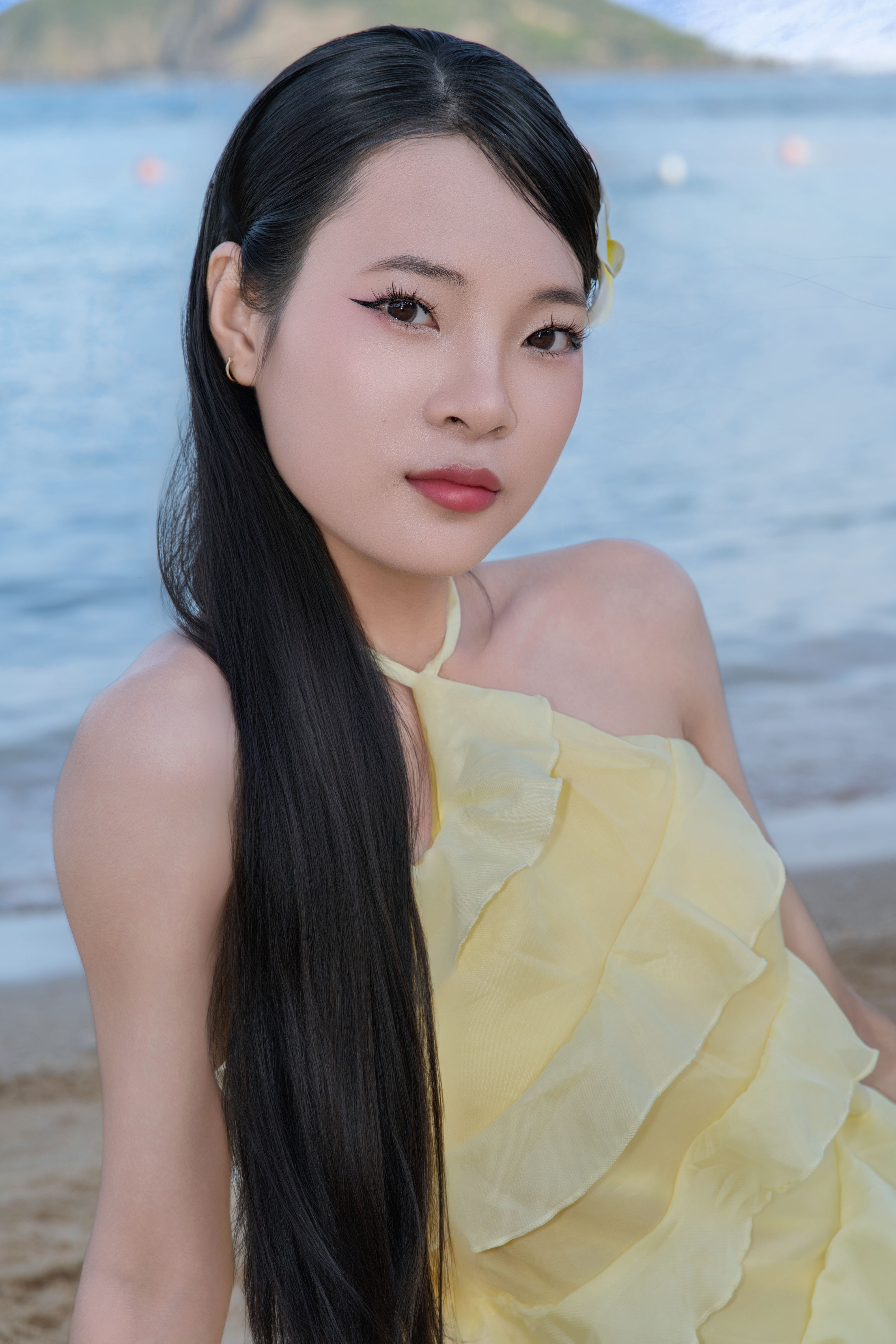 A woman wearing a yellow dress poses gracefully on a sandy beach, exuding elegance.