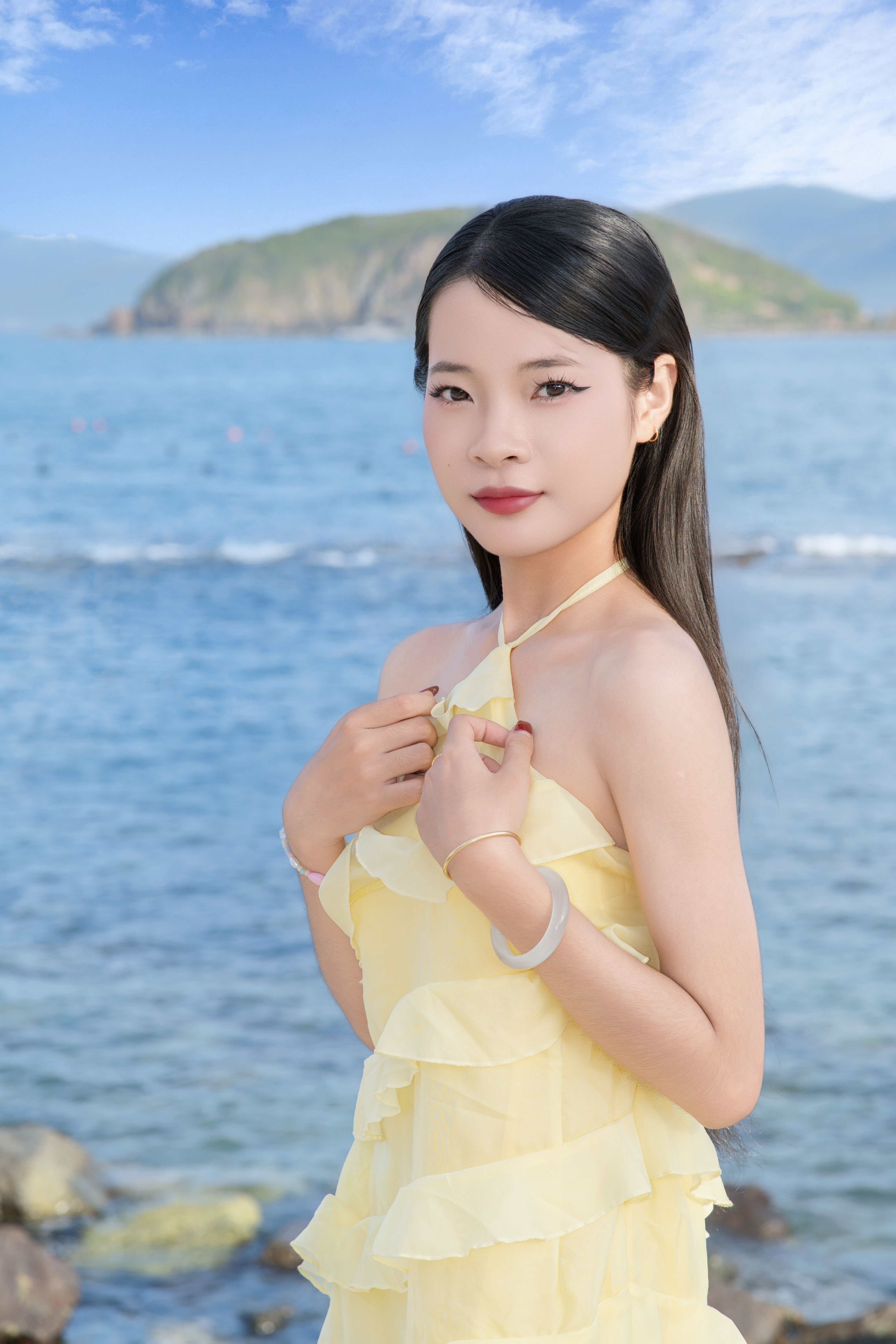 A young woman in a yellow dress poses gracefully by the seaside, capturing a serene summer moment.