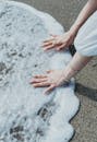 Hands Touching Gentle Ocean Waves on Sandy Beach