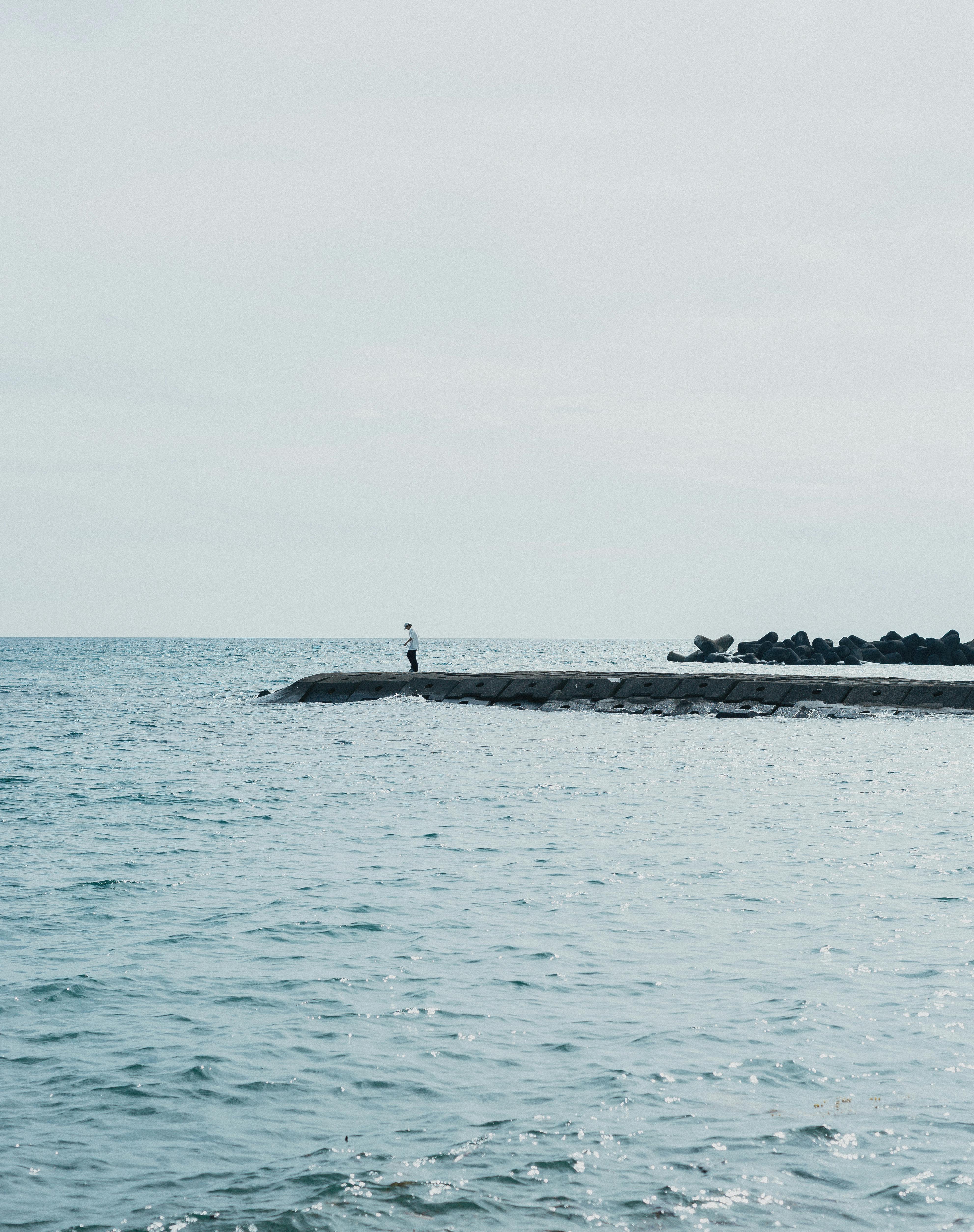 A lone person stands on a seaside pier in Nishiizu, Shizuoka, Japan, surrounded by calming ocean waters.