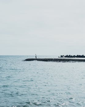A lone person stands on a seaside pier in Nishiizu, Shizuoka, Japan, surrounded by calming ocean waters.