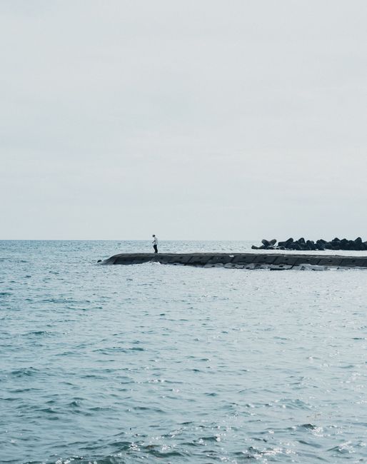 A lone person stands on a seaside pier in Nishiizu, Shizuoka, Japan, surrounded by calming ocean waters.