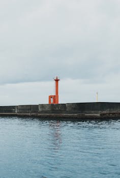 A red lighthouse stands on a sea wall in Nishiizu, Shizuoka, Japan, against a cloudy sky.