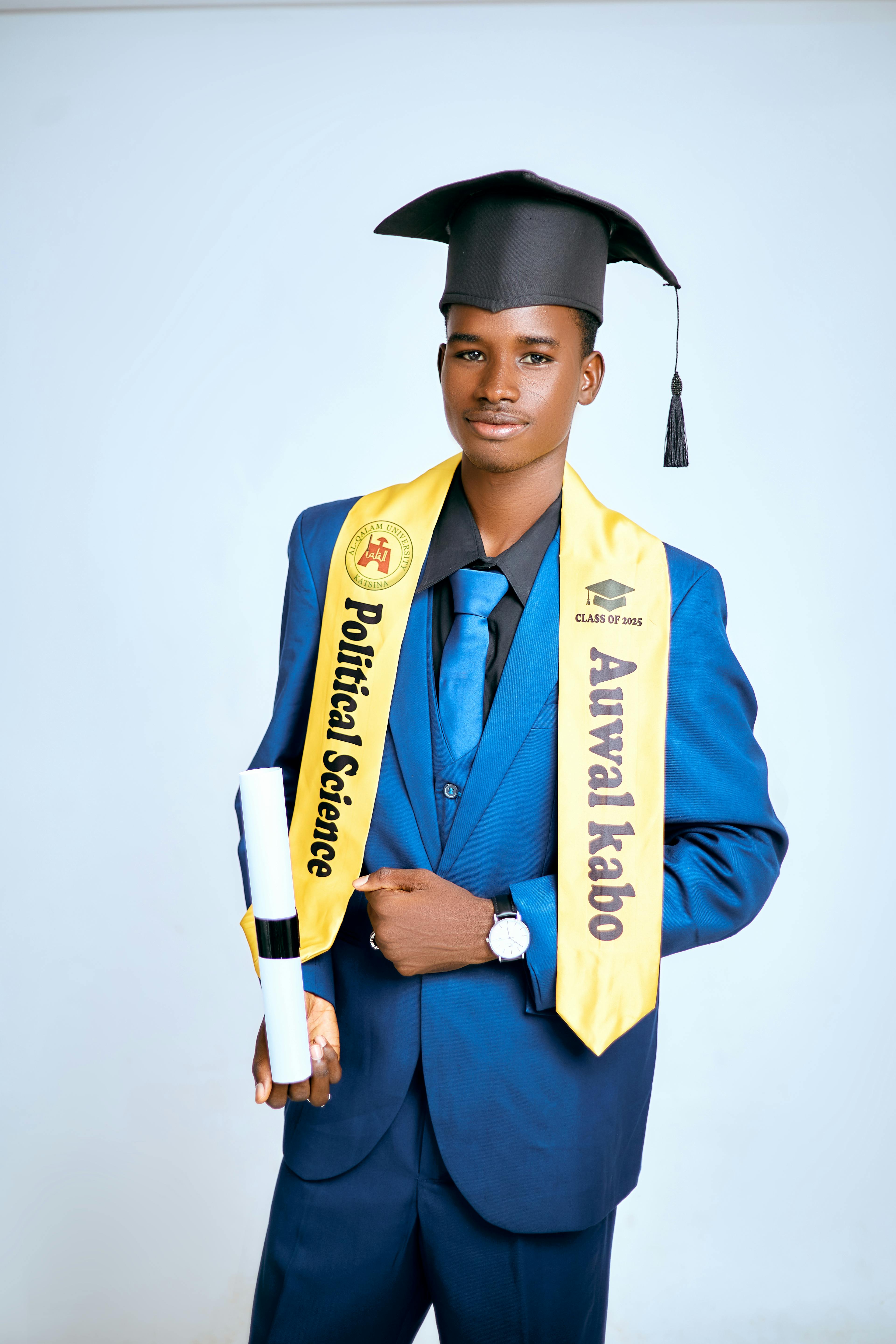 Young male graduate in blue suit and cap celebrating achievement with diploma.