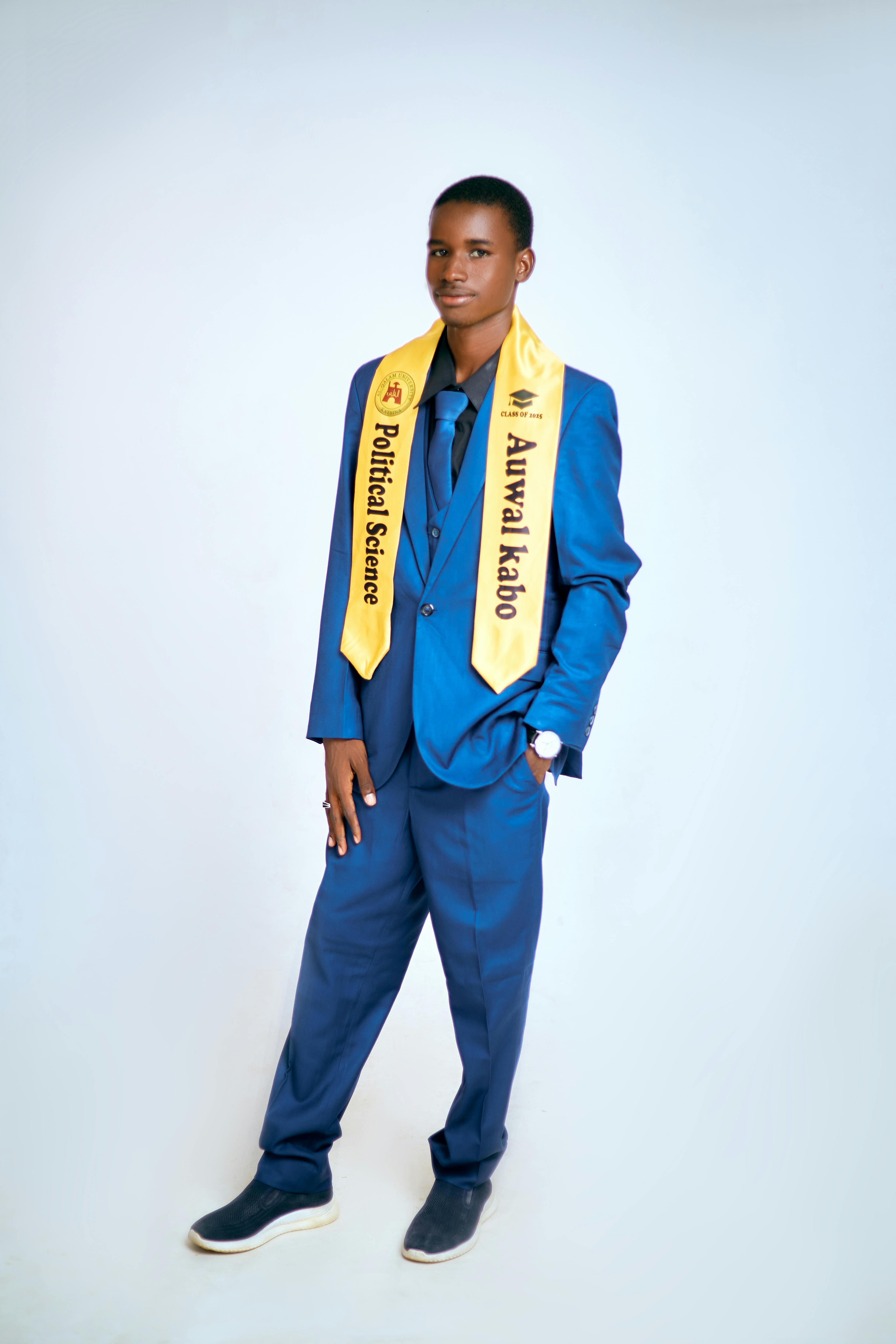 Young graduate in blue suit with a political science graduation sash, standing confidently.