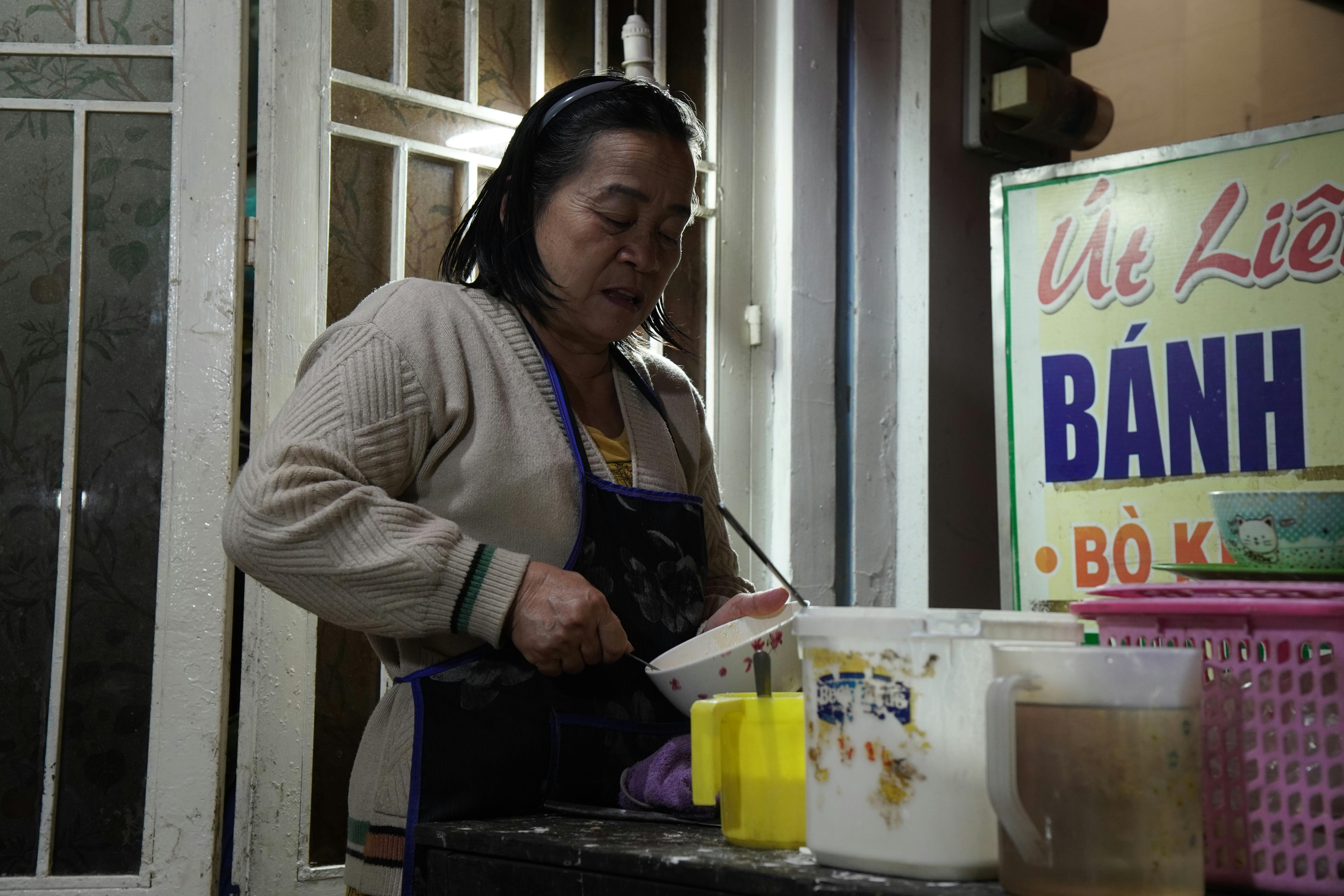 A woman preparing Vietnamese banh dish at a street vendor stall during the night.