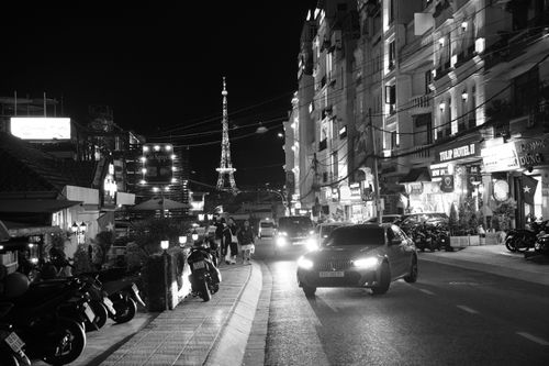 Free Black and white night scene of a busy city street featuring an Eiffel-like structure in the background. Stock Photo