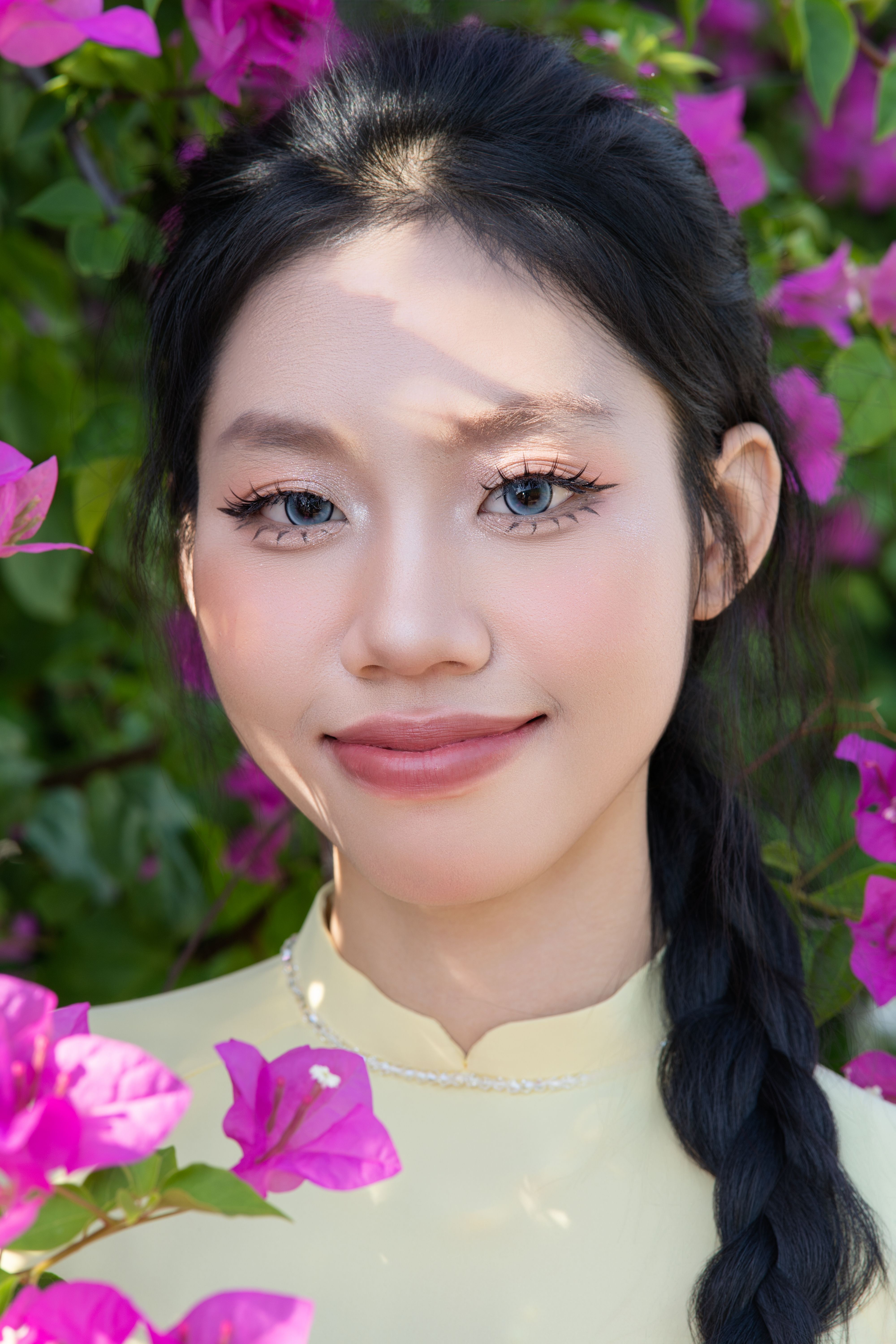 A young woman smiling amidst vibrant bougainvillea flowers, highlighting natural beauty and serenity.