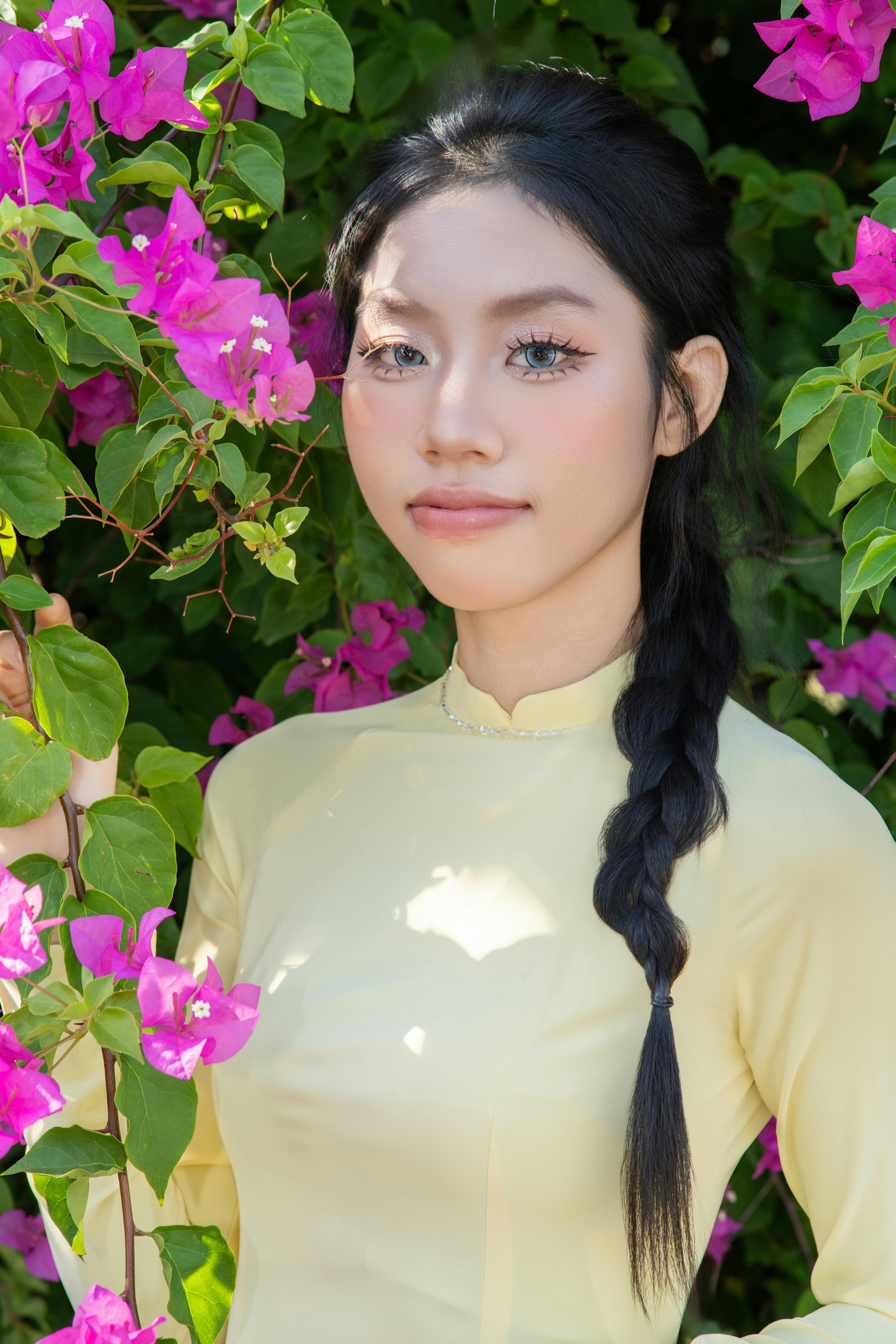 Young woman in a yellow dress poses elegantly amidst vibrant pink bougainvillea flowers.