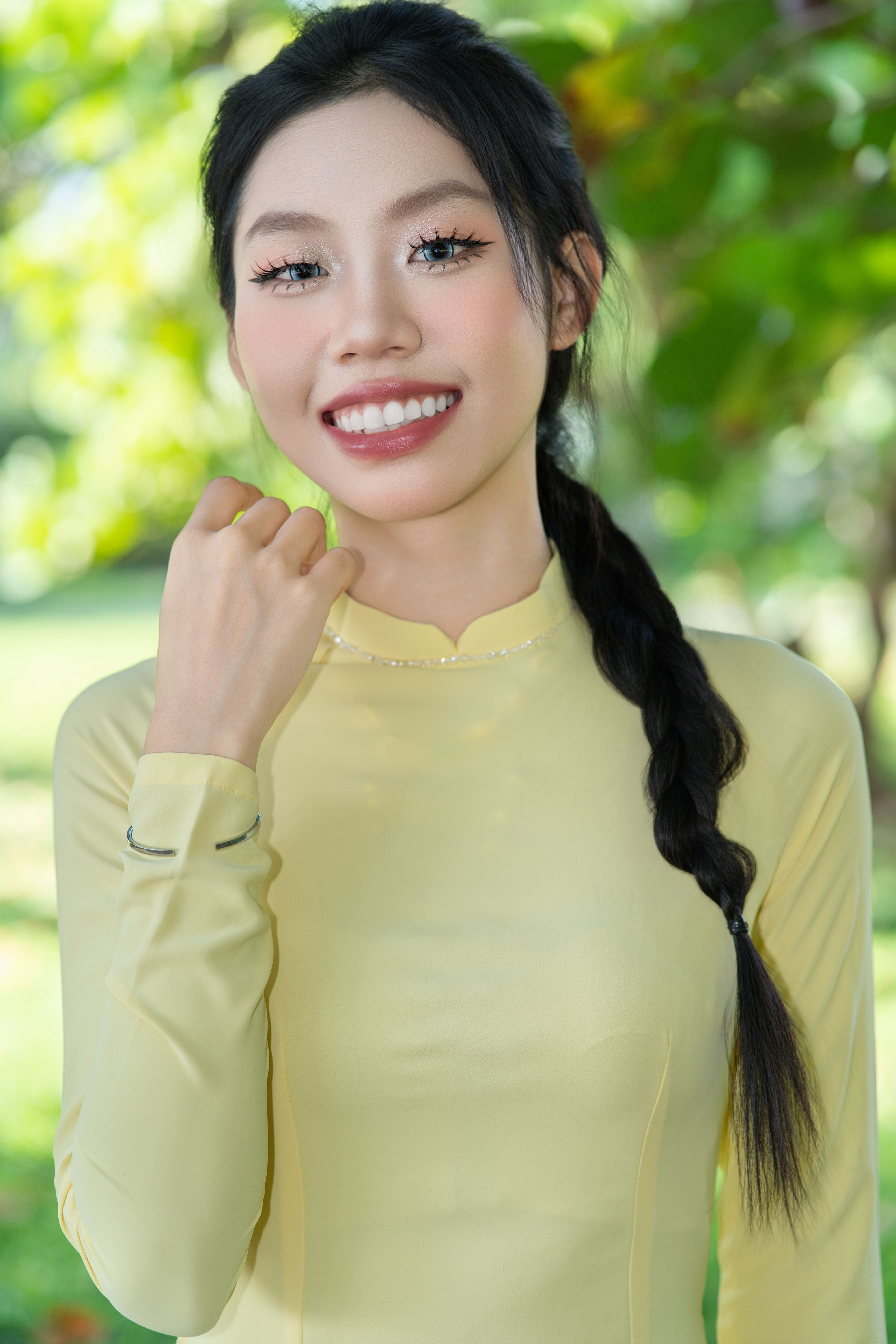 Woman in yellow traditional dress smiling in a sunny outdoor setting.