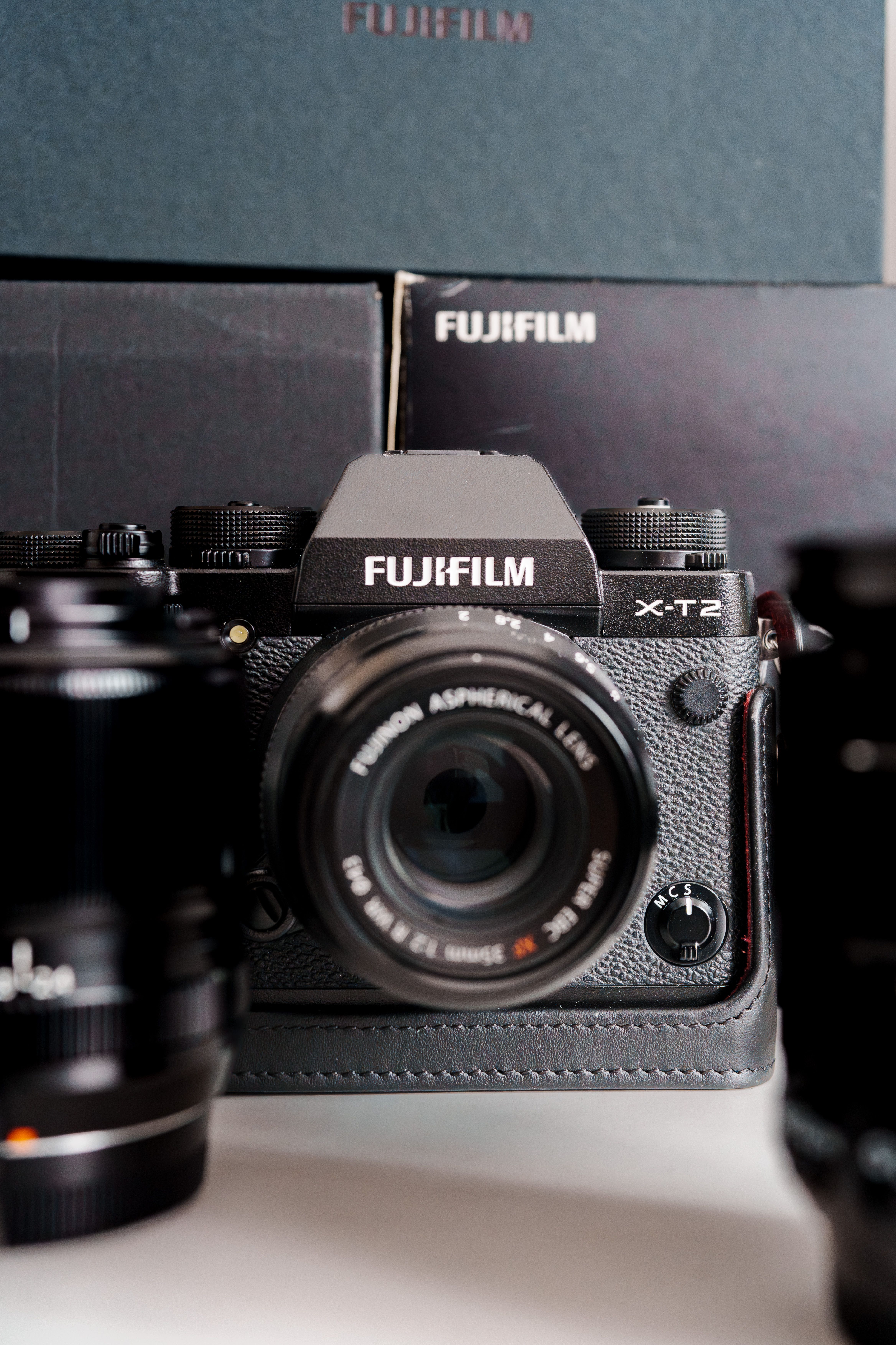 Fujifilm X-T2 camera with lens, surrounded by lenses and boxes, showcasing photography gear.