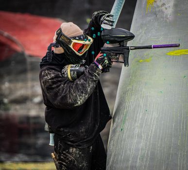 A paintball player in full gear taking aim during a competitive game outdoors.