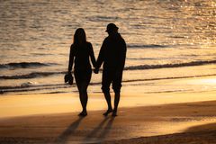 Silhouette of a couple walking hand in hand on a sunny beach at sunset.