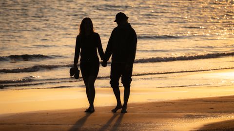 Silhouette of a couple walking hand in hand on a sunny beach at sunset.
