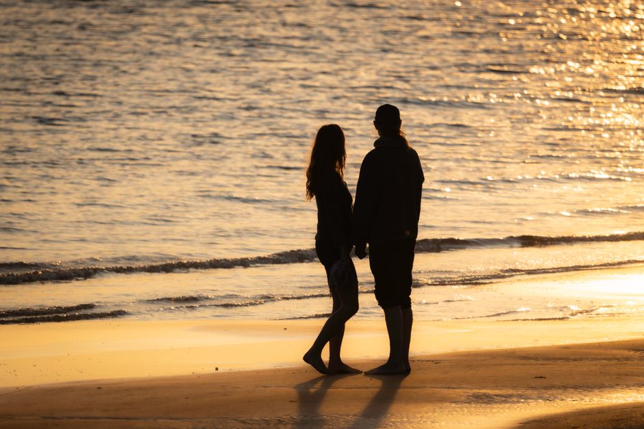 9-Day Tanzania Premium Honeymoon Safari – Romance in the Wild - Silhouetted couple stands on a sunlit beach during a serene sunset, capturing a romantic moment.