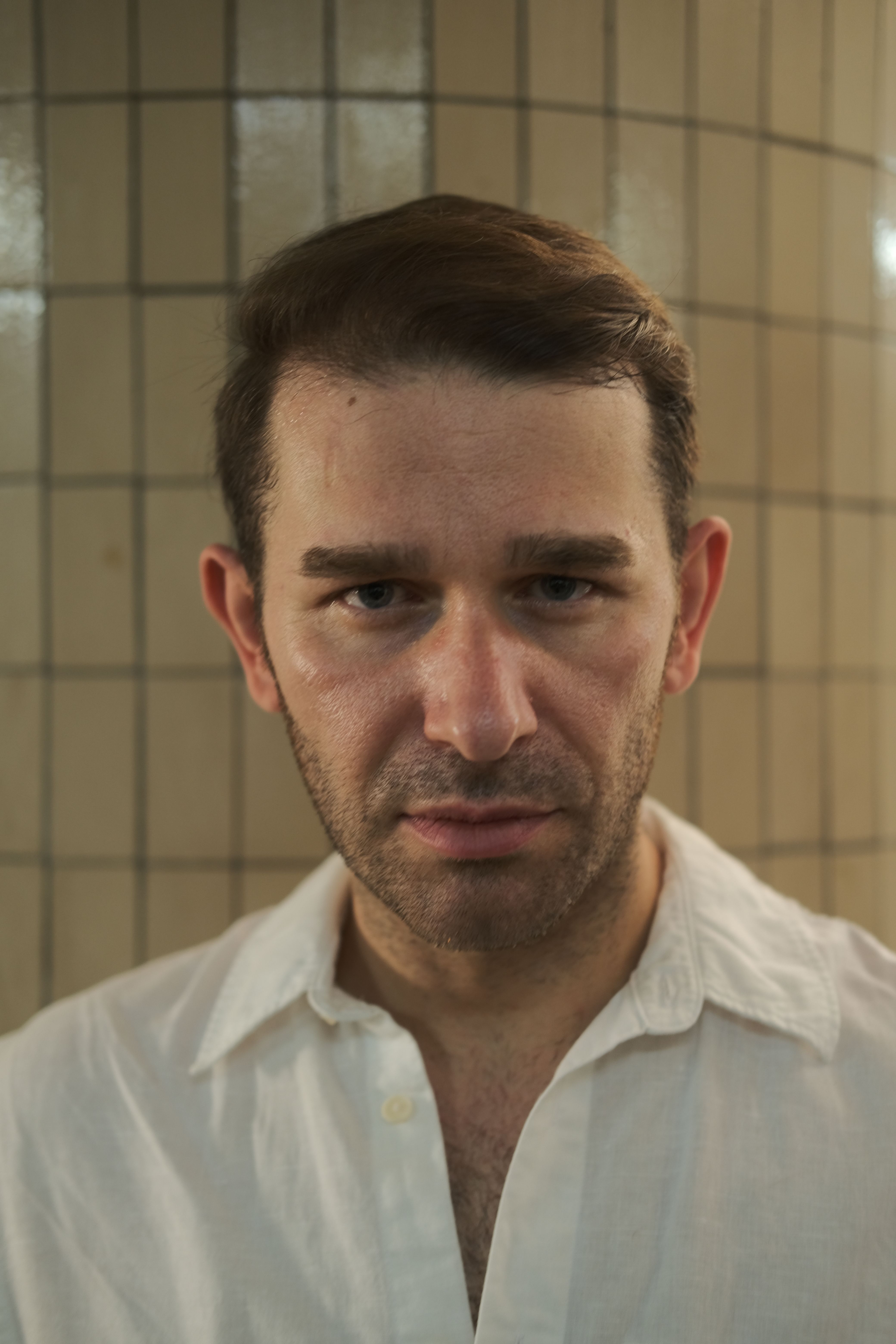 Close-up portrait of a man indoors with a neutral expression, wearing a white shirt.