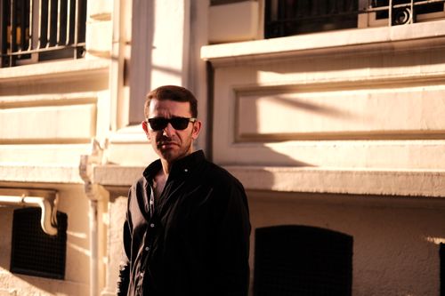 Free Stylish man in sunglasses standing in a sunlit urban alley wearing a black shirt. Stock Photo