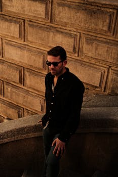 Stylish man wearing sunglasses stands on a stone staircase, captured during a warm evening glow.