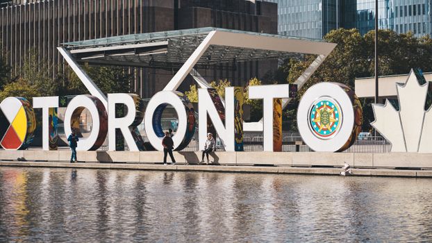 Iconic Toronto sign with people walking by, a popular tourist attraction in downtown Toronto.