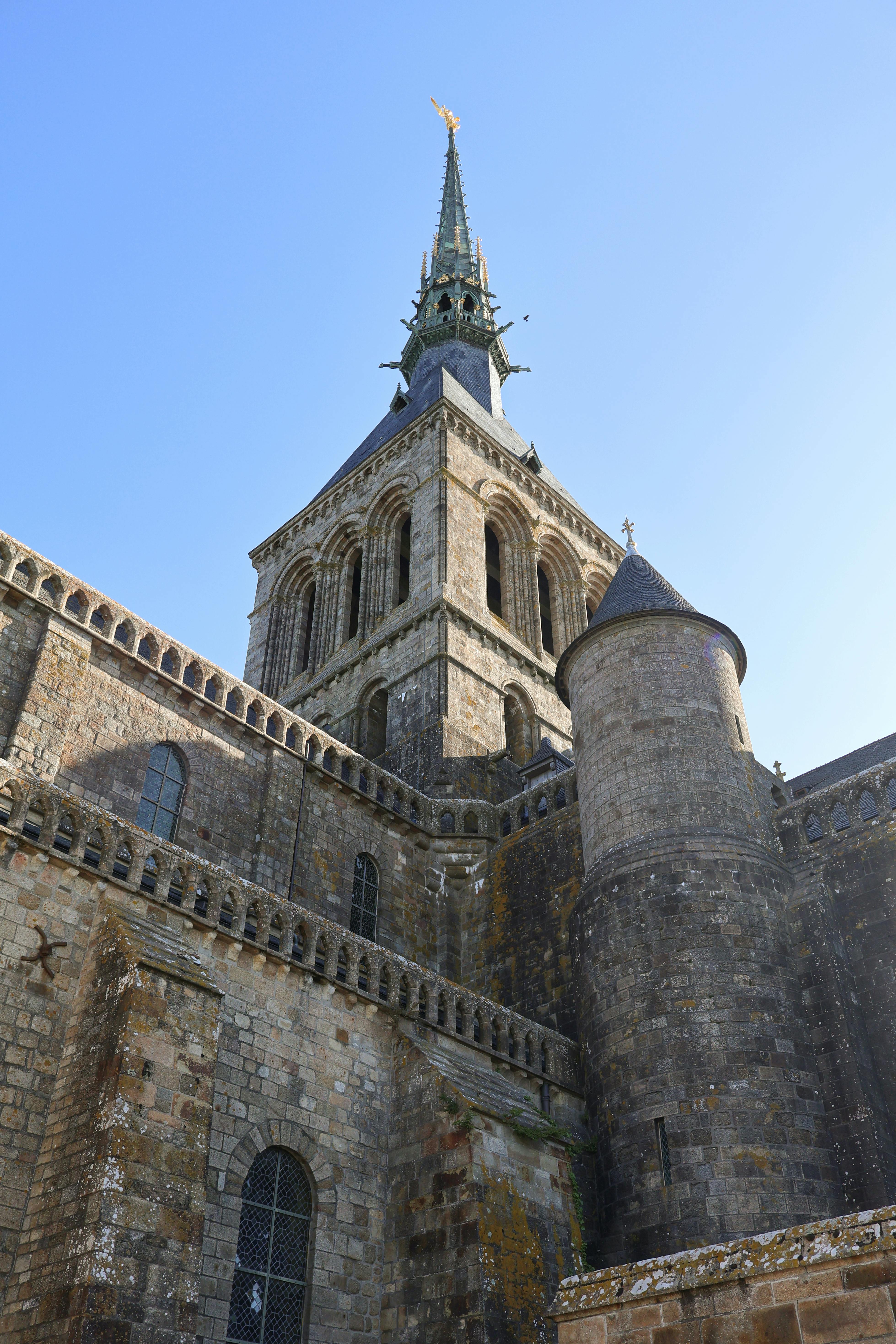 Ancient Mont Saint-Michel Abbey with spire against a clear blue sky in Normandy, France.