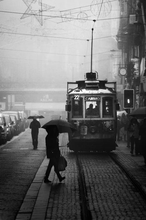 Фотография человека, переходящего улицу возле трамвая в оттенках серого