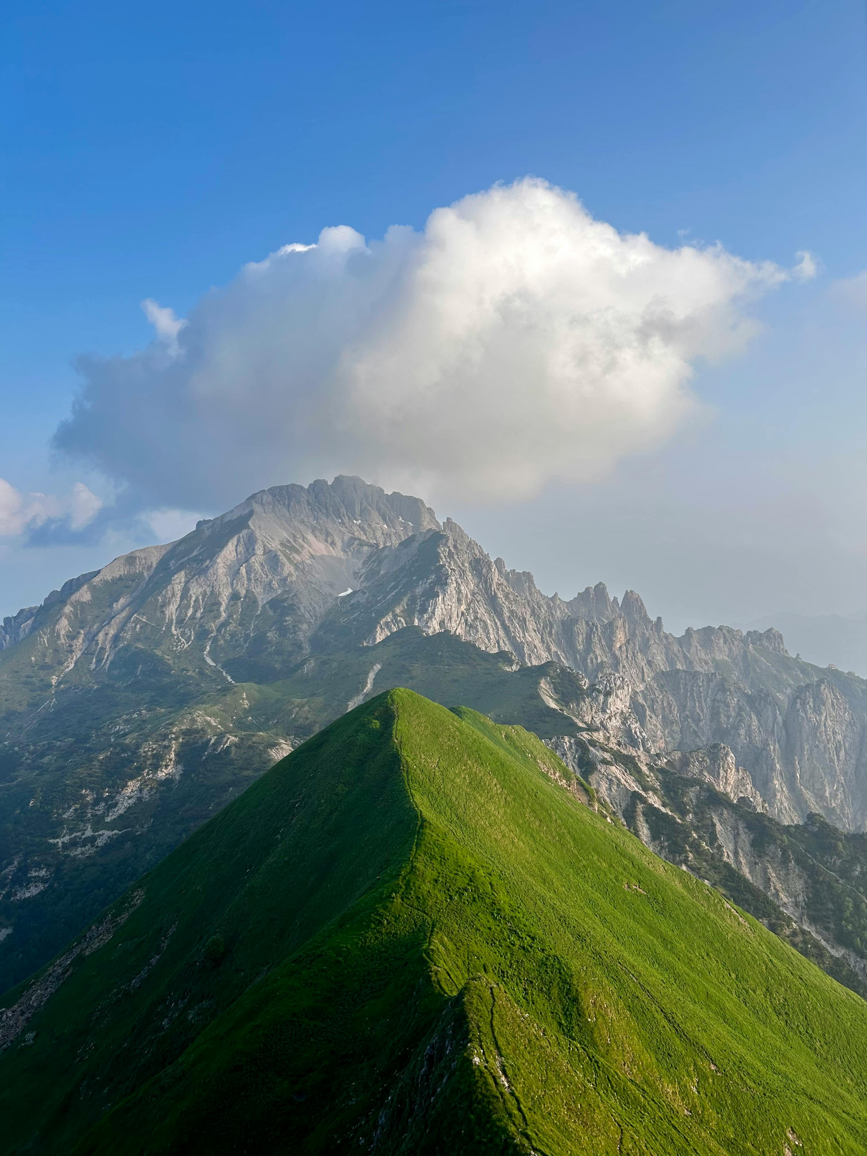 A breathtaking view of a green mountain peak against rugged cliffs under a bright blue sky.