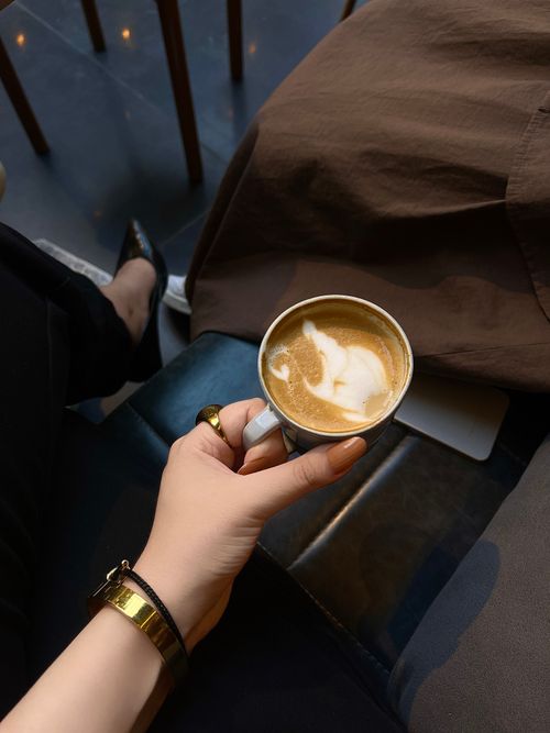 Free Hand holding a latte with cat latte art in a cozy cafe. Warm, inviting atmosphere. Stock Photo