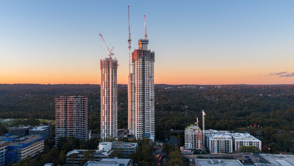 Aerial view of skyscrapers being constructed at sunset, surrounded by urban and forest landscape in Chatswood, Australia.