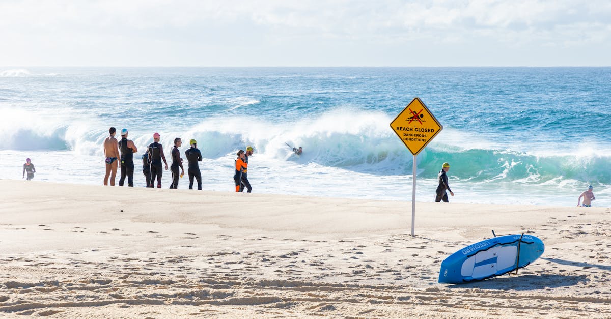 Photo by Macourt Media Group of surfers on a beach with a 'Beach Closed' sign and waves in the background.