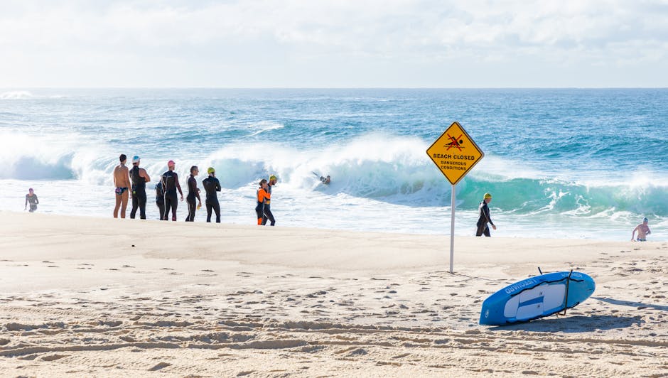 Photo by Macourt Media Group of surfers on a beach with a 'Beach Closed' sign and waves in the background.