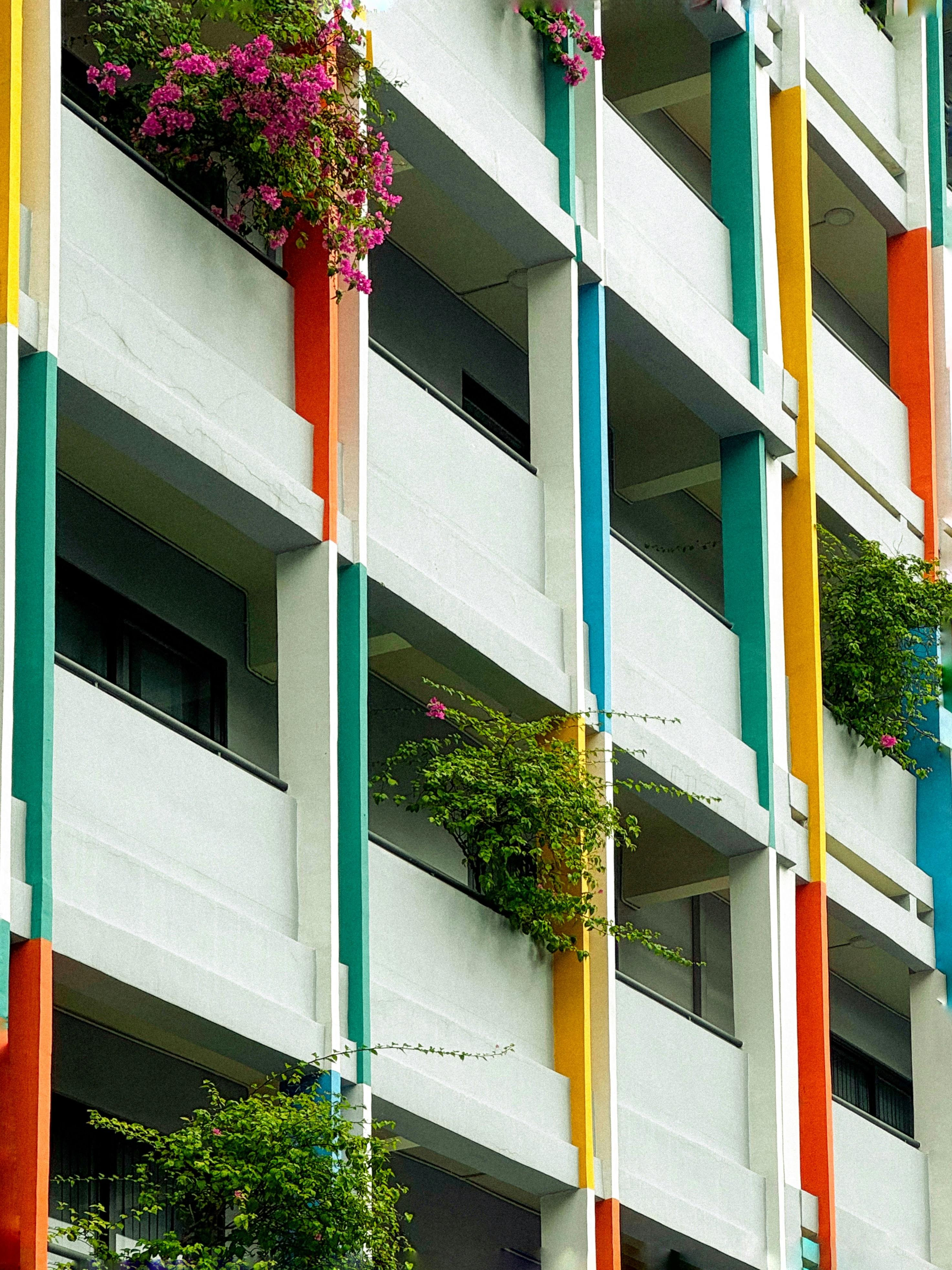 Colorful apartment facade with lush greenery on balconies, creating a vibrant urban aesthetic.