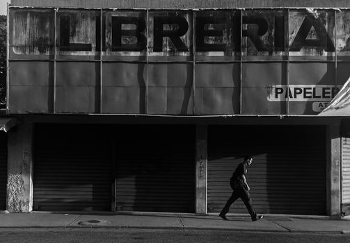 Black and white photo of a person walking past a closed bookstore with weathered signage.
