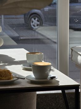 A warm morning scene inside a cafe with coffee cups and dessert.