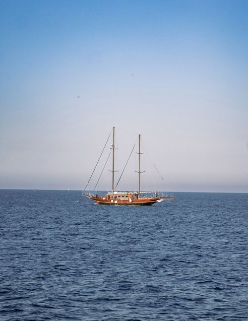 Free A calm ocean with a sailing boat under a clear blue sky, perfect for travel and adventure themes. Stock Photo