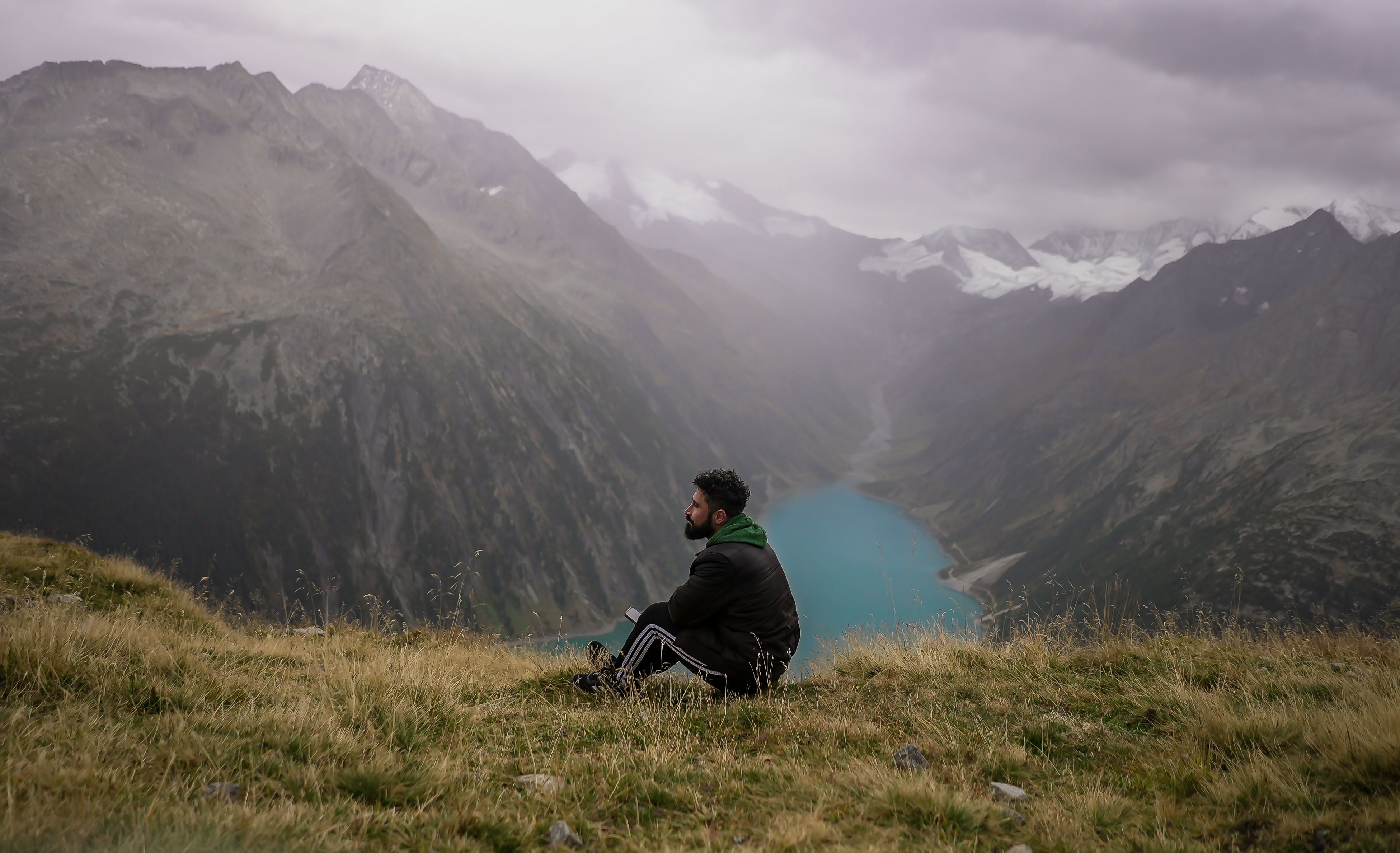 Man sitting on a grassy hill, overlooking a serene lake and majestic mountains in Tyrol, Austria.