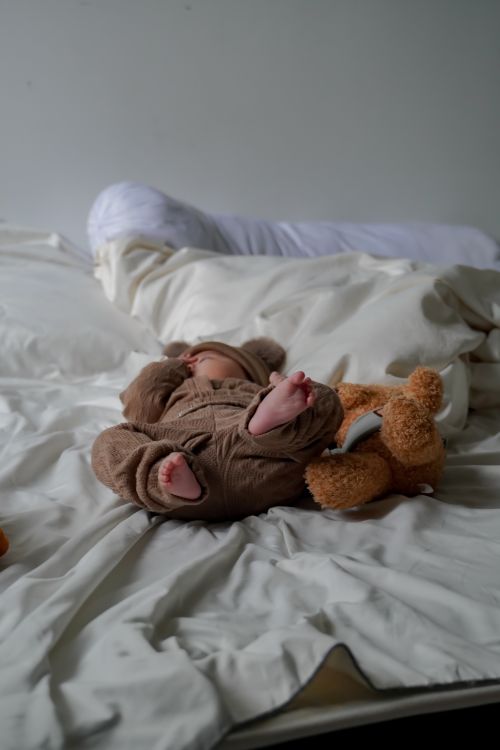 Free A baby peacefully sleeps with a teddy bear on a soft bed, creating a serene and comforting scene. Stock Photo