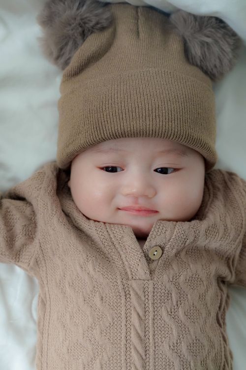 Free Smiling baby wearing a cozy knit outfit with bear ear hat, lying on a soft white blanket. Stock Photo
