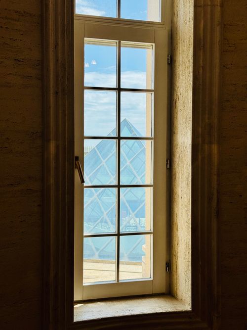 Free Serene view of Louvre Pyramid framed by a classic window, blending art and architecture. Stock Photo