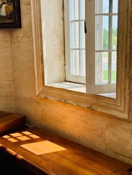 Warm sunlight streams through an open rustic window, casting shadows on a wooden interior.