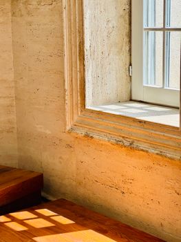 A beautifully sunlit window casting shadows on a rustic interior wall and wooden stairs.