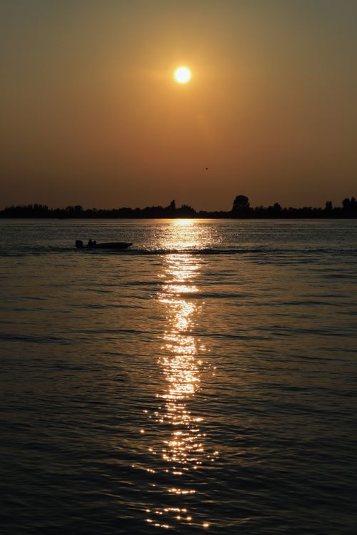 Free Silhouette of a boat during sunset over a tranquil lake. Stock Photo