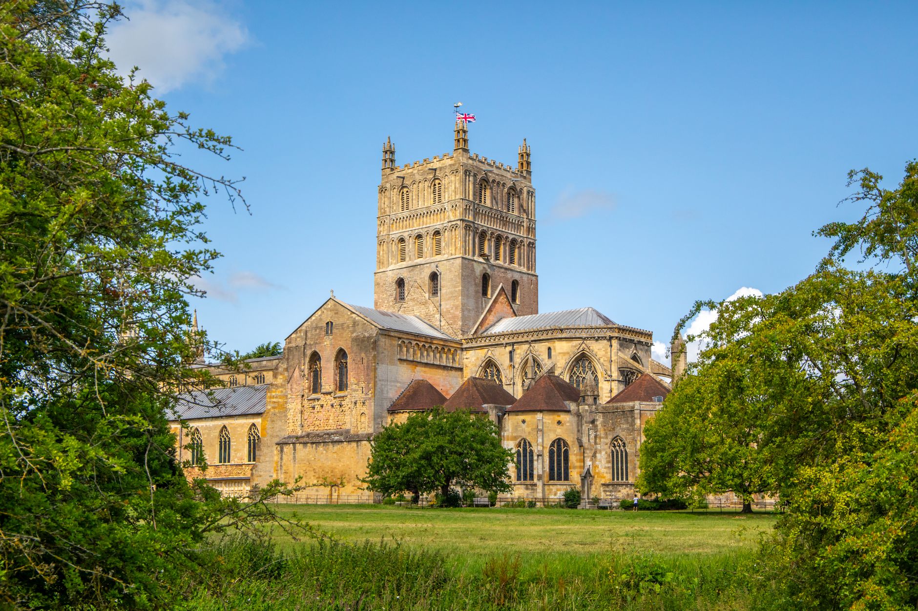Tewkesbury Abbey surrounded by green trees and historic architecture on a sunny day, England